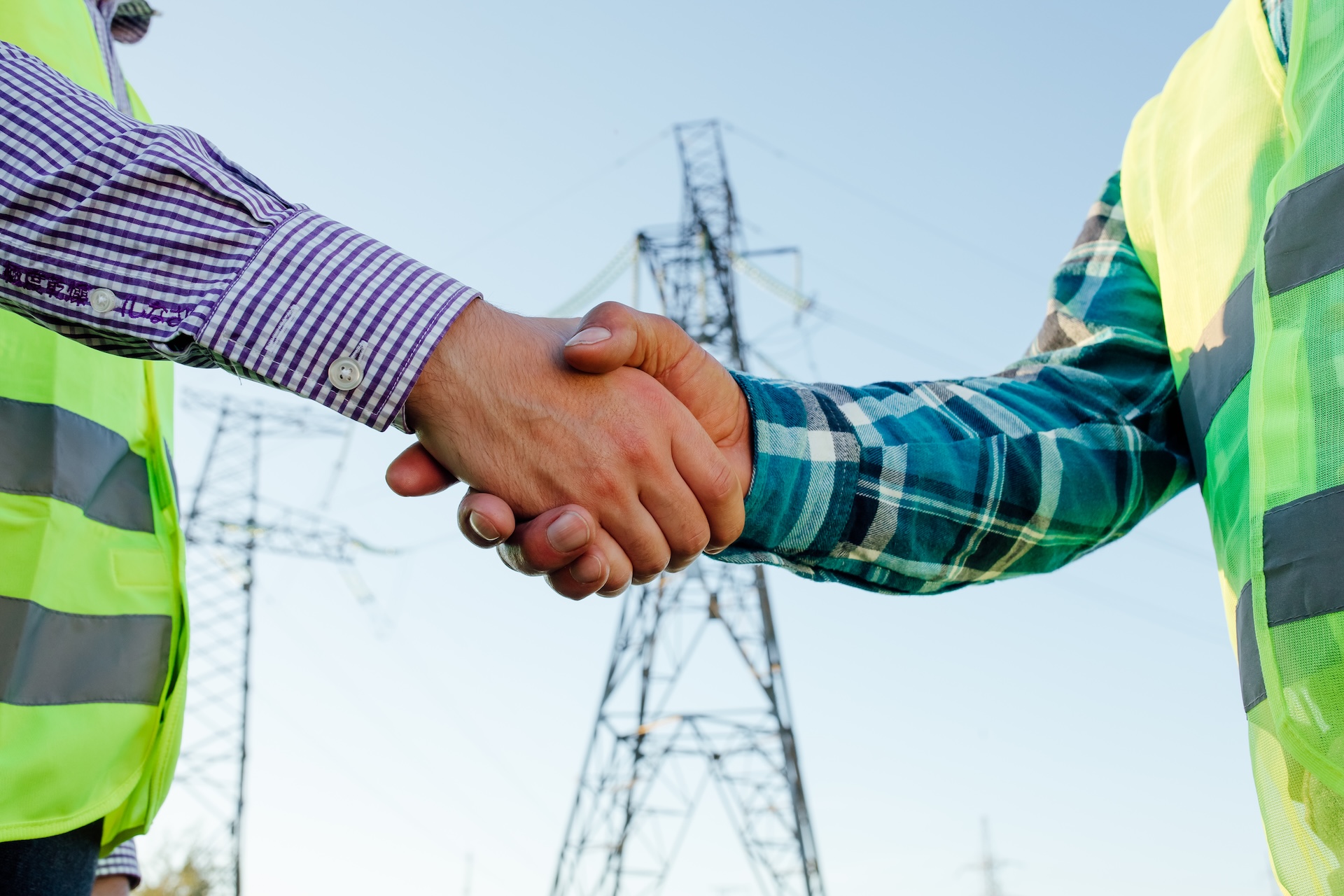 Engineers shaking hands against high voltage tower